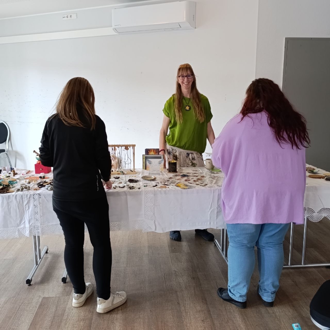 spirituelle Produkte werden an einem Verkaufsstand verkauft. link und rechts stehen interessierte Kunden, mittig Barbara Mazur